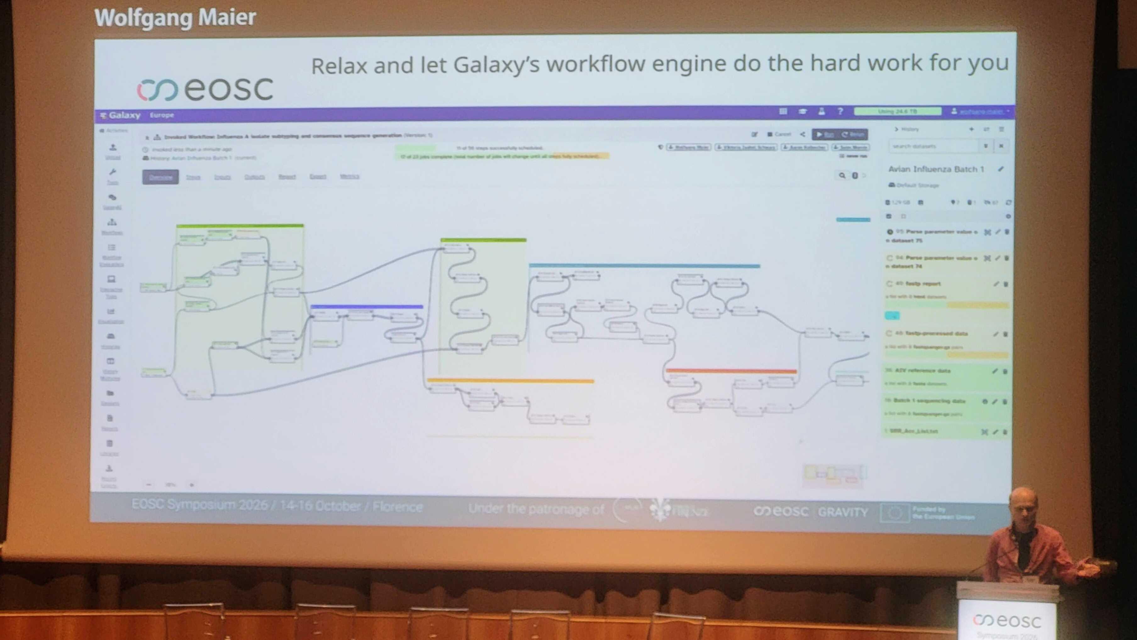 Wolfgang at the stage of the auditorium of the Palazzo dei Congressi presenting a slide showing a complex Galaxy workflow invocation titled: "Relax and let Galaxy's workflow engine do the hard work for you"